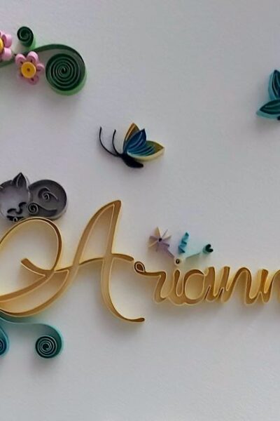 quilling corsivo, il nome Arianna scritto con strisce di carta gialle e personalizzato con farfalle e piccoli fiori